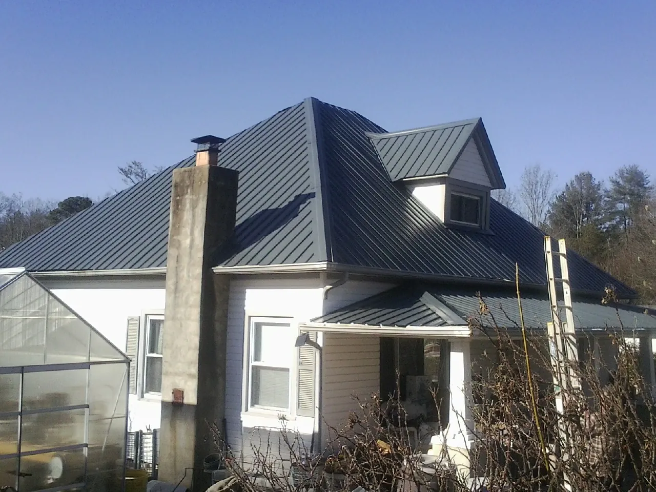 Dark blue standing seam metal roof on a white farmhouse with dormer — Slate & Tile Roof Repair by Roofing Brothers in Bulger