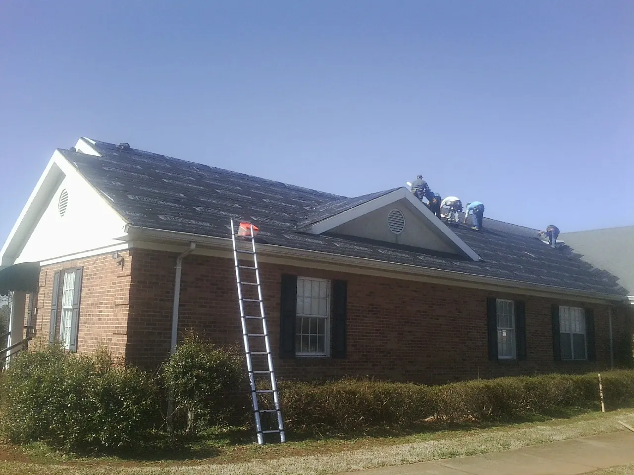 Crew tearing shingles off a brick ranch roof with a ladder set — Metal Roof Repair work by our crew in Bulger