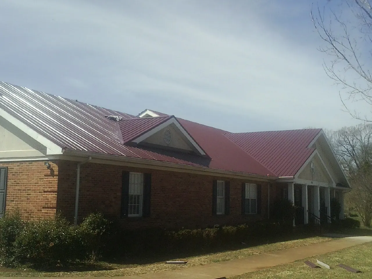 Red metal roof with gabled entries on a long brick building, from a Hail Damage Roof Repair job in Bulger