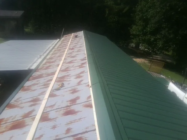 Old rusted panels beside newly installed green metal roofing — Wind Damage Roof Repair by Roofing Brothers in Bulger