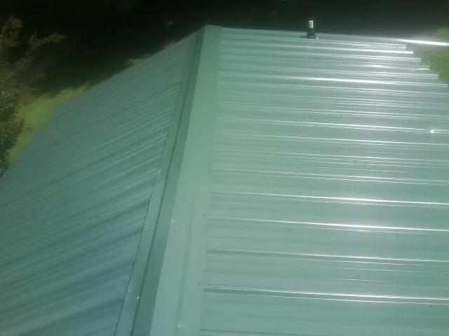 New green metal panels meeting at the ridge of a roof — Flat Roof Repair work by our crew in Bulger