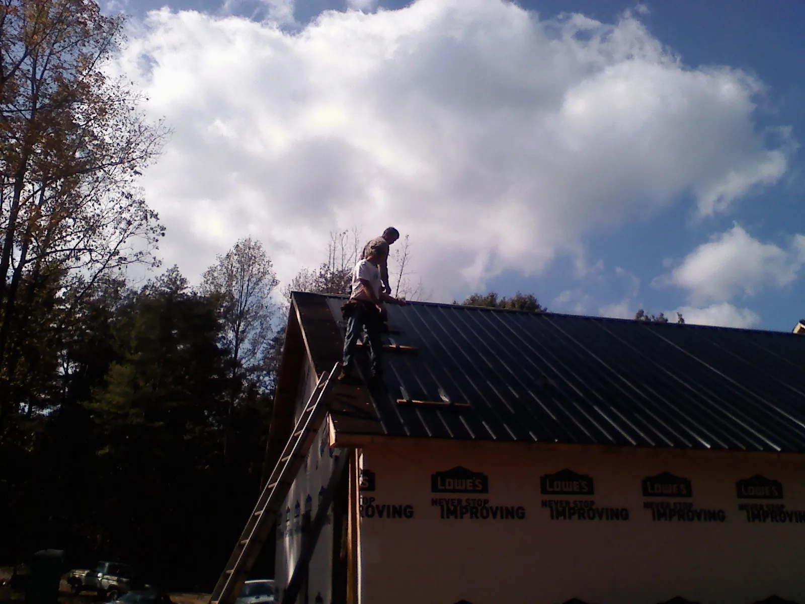 Roofer fastening dark metal panels high against a cloudy sky, from a Roof Inspection job in Bulger