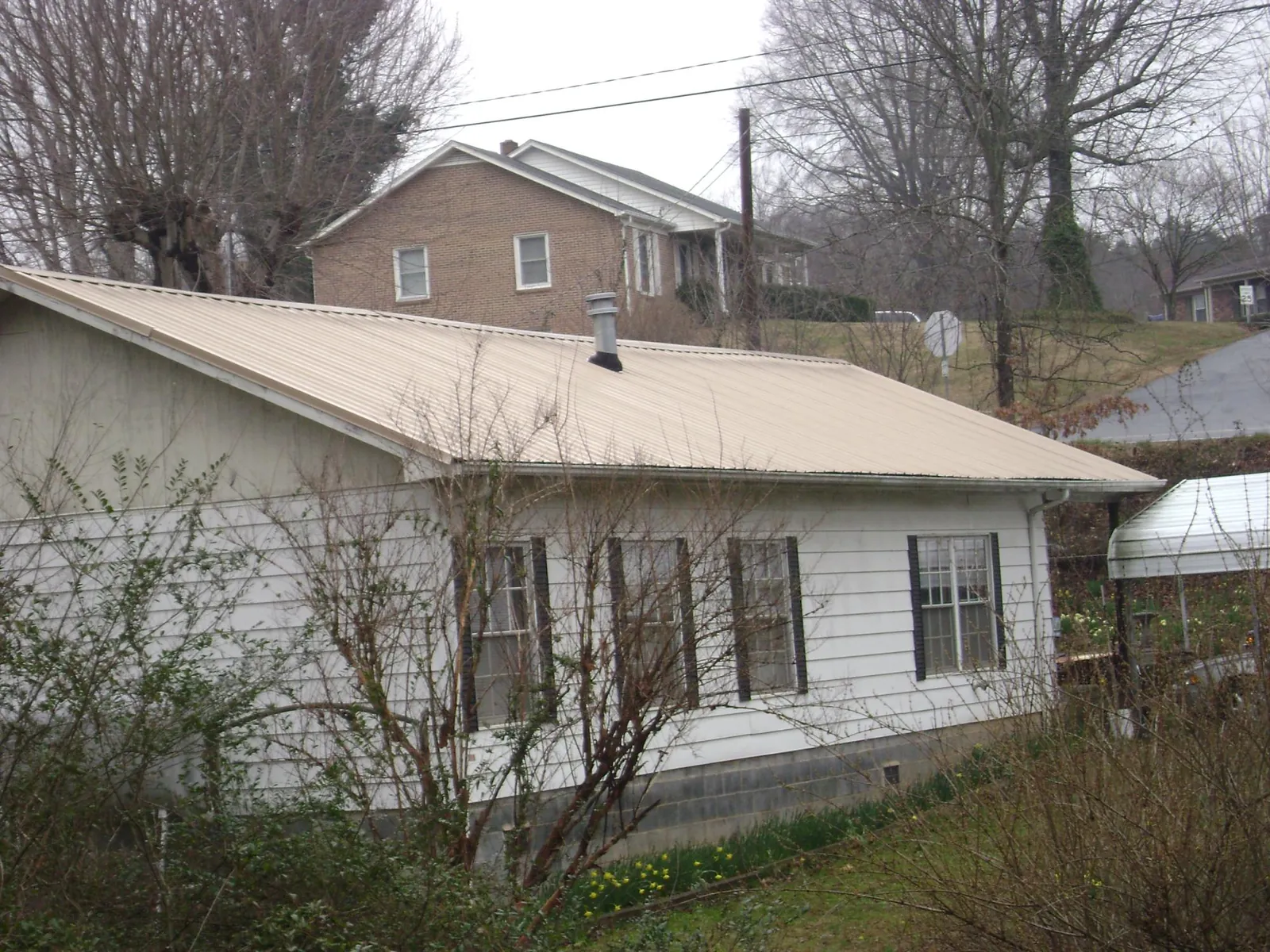 Tan metal roof on a white sided house set into a hillside — Commercial Roofing by Roofing Brothers in Bulger