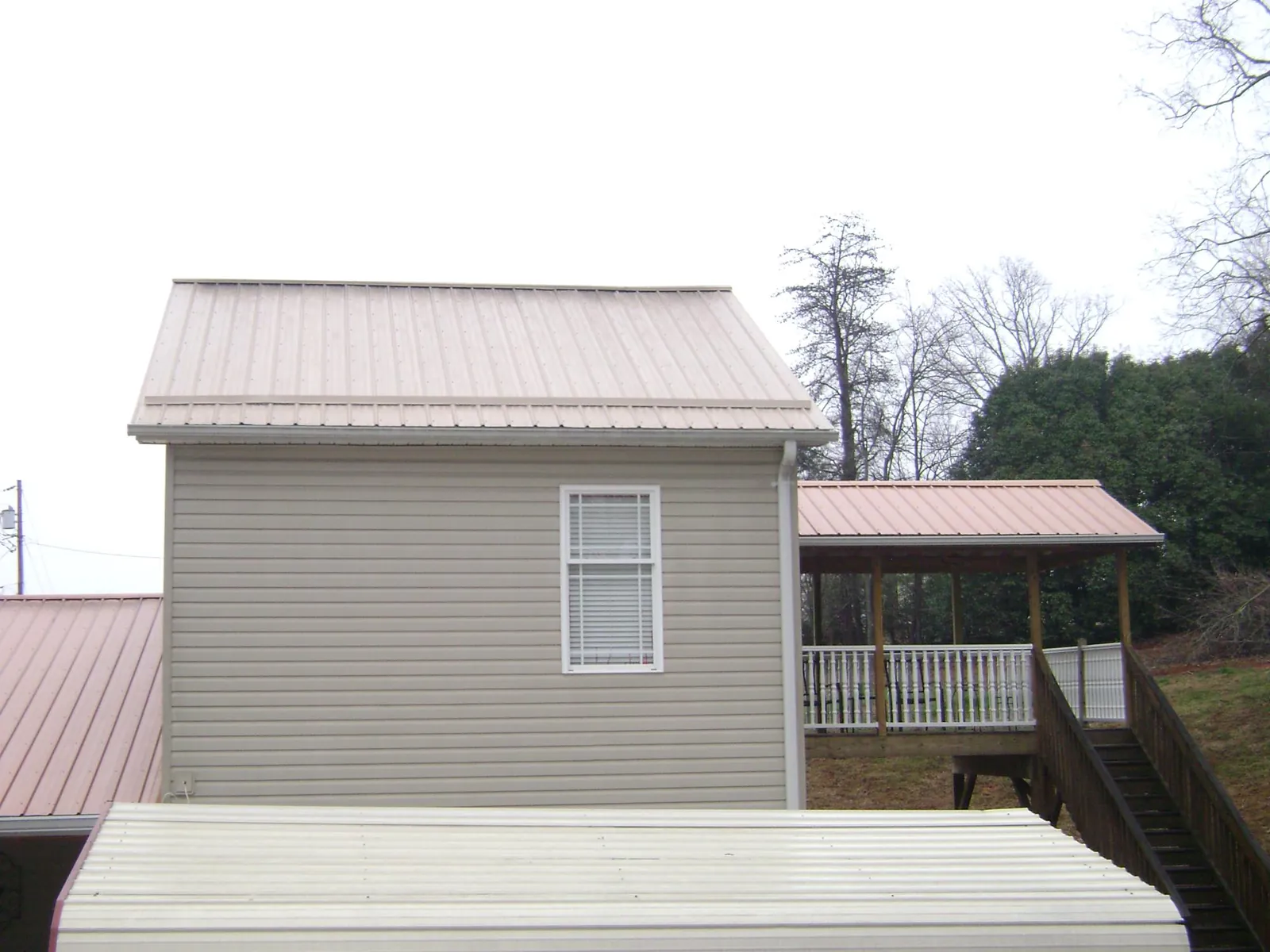 Tan metal roofs on a two story addition and attached porch, from a Roof Replacement job in Bulger